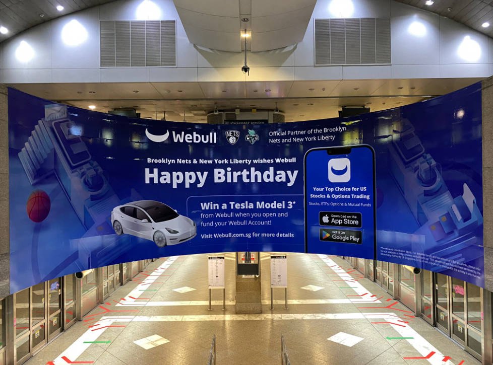 Webull birthday campaign on the curved ambient wall above the escalators at Bugis MRT concourse